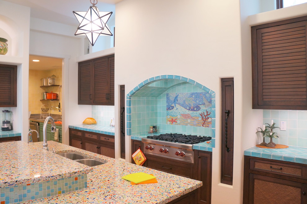 タンパにあるラグジュアリーな広いビーチスタイルのおしゃれなキッチン (アンダーカウンターシンク、ルーバー扉のキャビネット、茶色いキャビネット、再生ガラスカウンター、青いキッチンパネル、モザイクタイルのキッチンパネル、シルバーの調理設備、テラコッタタイルの床、オレンジの床) の写真