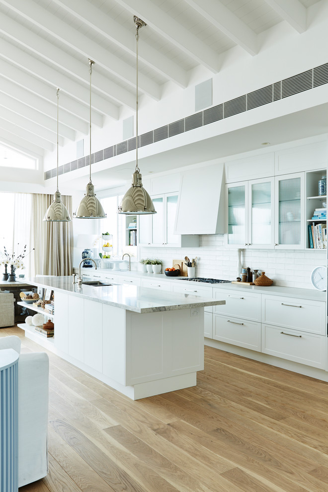 Inspiration for a large nautical single-wall open plan kitchen in Sydney with shaker cabinets, white cabinets, engineered stone countertops, white splashback, ceramic splashback, an island and grey worktops.