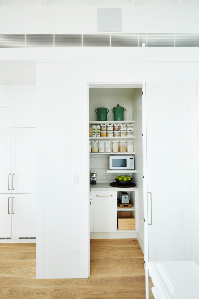 Diseño de cocina lineal costera grande abierta con armarios estilo shaker, puertas de armario blancas, encimera de cuarzo compacto, salpicadero blanco, salpicadero de azulejos de cerámica, una isla y encimeras grises