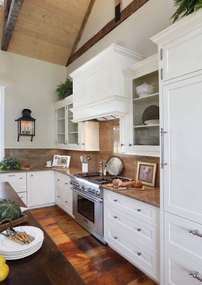 Foto på ett stort lantligt brun l-kök, med vita skåp, stänkskydd i sten, integrerade vitvaror, en rustik diskho, luckor med profilerade fronter, granitbänkskiva, mörkt trägolv, en köksö och brunt golv