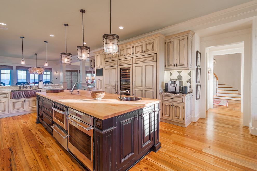 Example of a large transitional u-shaped light wood floor and brown floor eat-in kitchen design in Charleston with a farmhouse sink, beaded inset cabinets, white cabinets, an island, wood countertops, multicolored backsplash, stone tile backsplash and paneled appliances