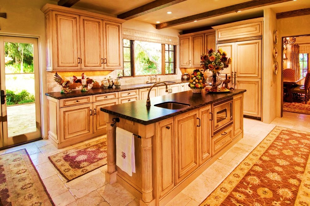 Foto på ett litet rustikt kök, med en undermonterad diskho, luckor med profilerade fronter, beige skåp, bänkskiva i täljsten, beige stänkskydd, stänkskydd i stenkakel, integrerade vitvaror, travertin golv och en köksö