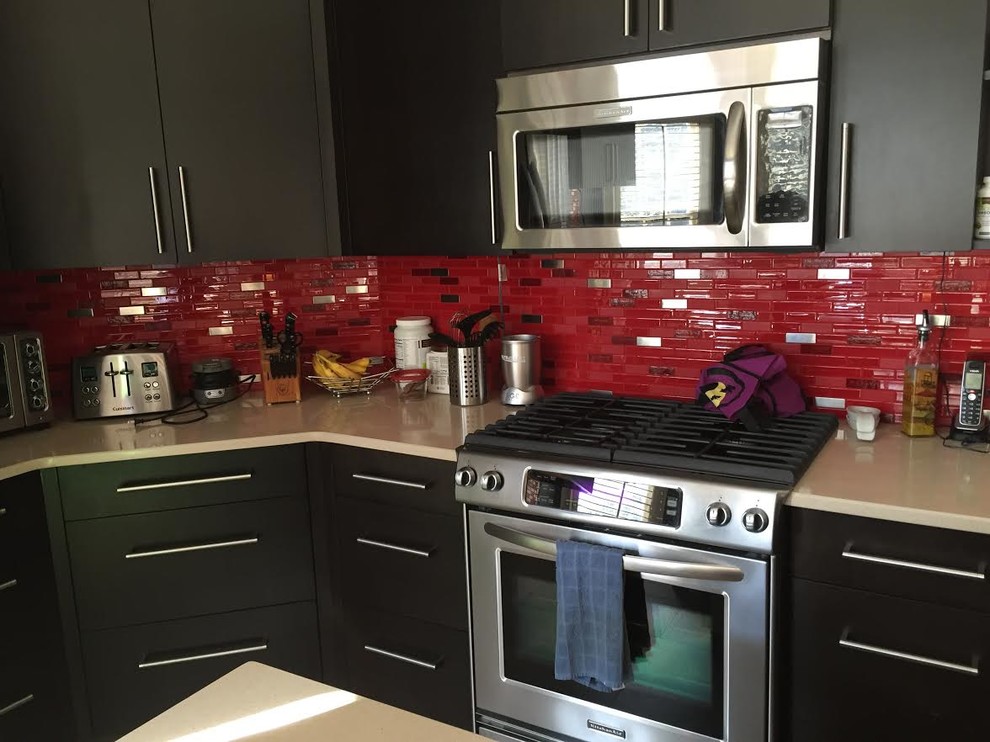 Foto di una cucina design di medie dimensioni con ante nere, paraspruzzi rosso, paraspruzzi con piastrelle di vetro e elettrodomestici in acciaio inossidabile