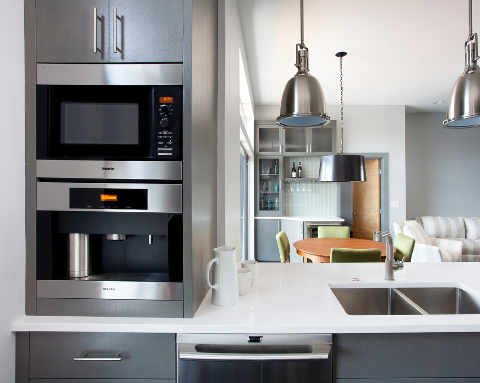 На фото: кухня-гостиная в современном стиле с плоскими фасадами, серыми фасадами, белым фартуком, техникой из нержавеющей стали, фартуком из стеклянной плитки и двойной мойкой