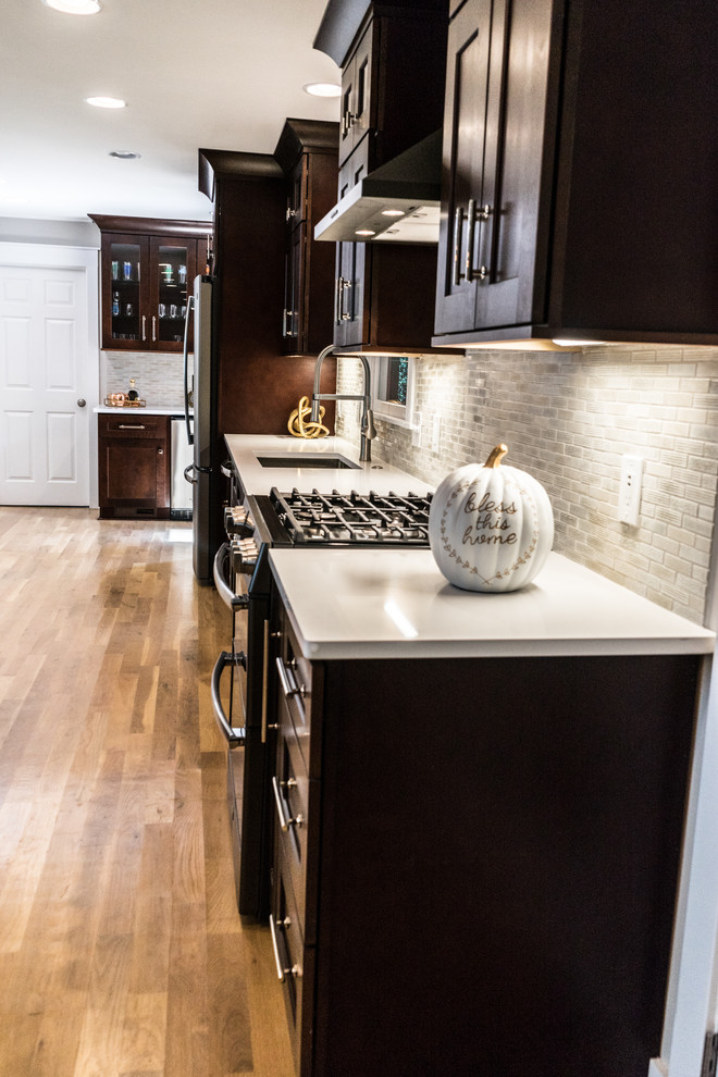 This is an example of a large classic l-shaped kitchen in Atlanta with a submerged sink, shaker cabinets, dark wood cabinets, grey splashback, cement tile splashback, stainless steel appliances, light hardwood flooring, an island, brown floors and white worktops.