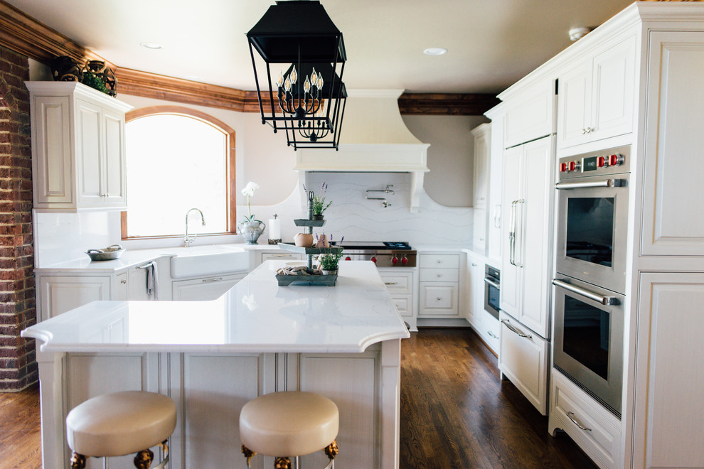 Large minimalist u-shaped dark wood floor and brown floor kitchen photo in Birmingham with a farmhouse sink, raised-panel cabinets, white cabinets, quartzite countertops, white backsplash, stainless steel appliances and an island