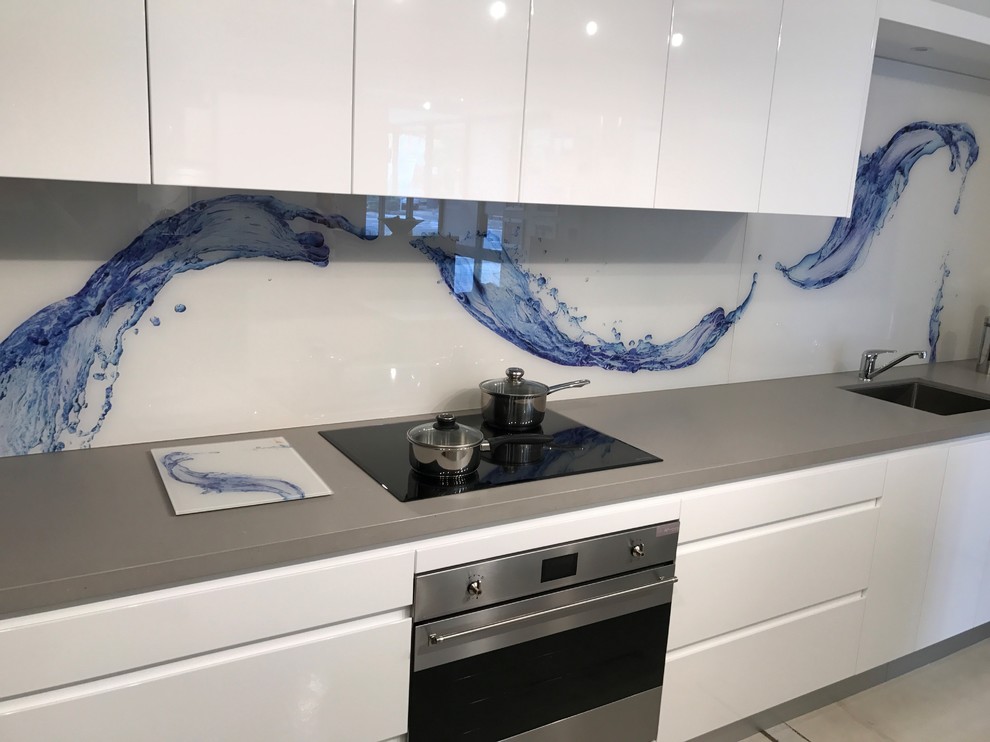 Foto på ett funkis linjärt kök och matrum, med en undermonterad diskho, flerfärgad stänkskydd, glaspanel som stänkskydd, rostfria vitvaror och en köksö