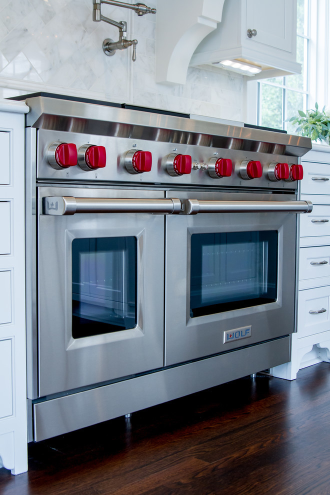 Immagine di una cucina abitabile chic con ante a filo, ante bianche, paraspruzzi bianco e elettrodomestici in acciaio inossidabile