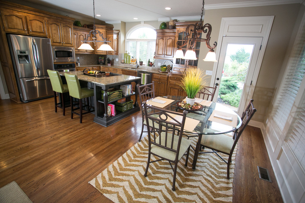 Eat-in kitchen - mid-sized traditional l-shaped medium tone wood floor eat-in kitchen idea in Kansas City with an undermount sink, raised-panel cabinets, medium tone wood cabinets, granite countertops, beige backsplash, ceramic backsplash, stainless steel appliances and an island