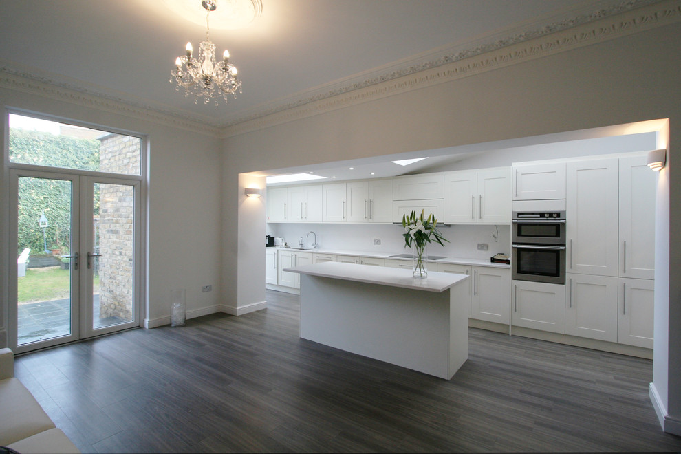 Medium sized contemporary galley kitchen/diner in London with a submerged sink, recessed-panel cabinets, white cabinets, granite worktops, white splashback, stainless steel appliances and an island.