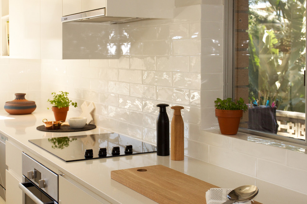 Modern inredning av ett avskilt, litet l-kök, med en undermonterad diskho, släta luckor, vita skåp, bänkskiva i kvarts, vitt stänkskydd, stänkskydd i keramik, vita vitvaror och klinkergolv i keramik