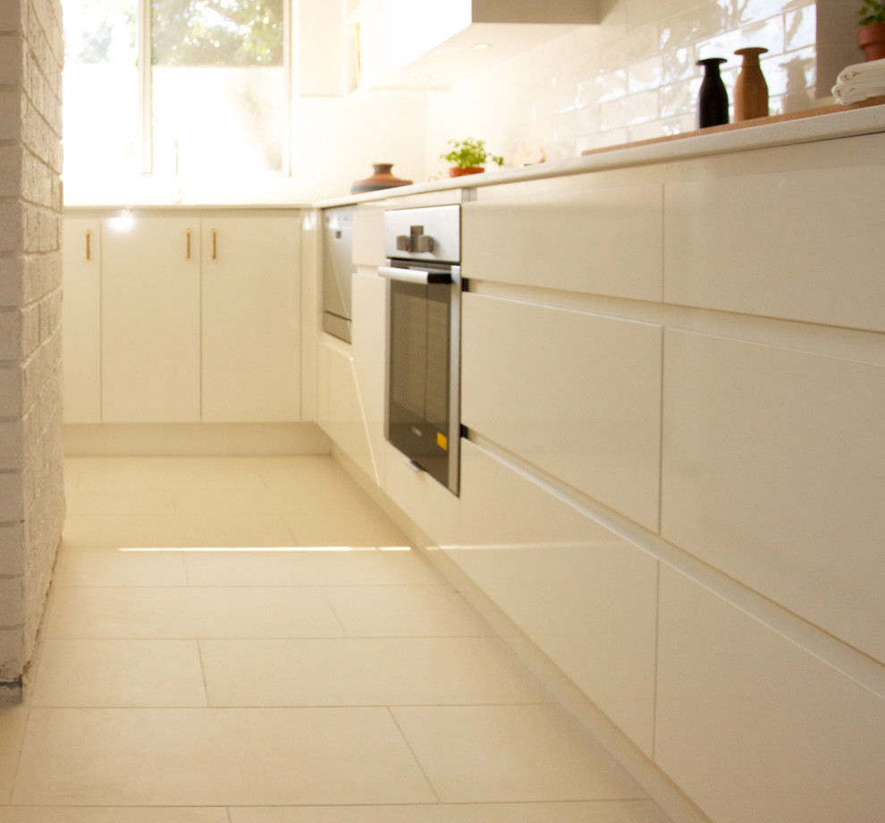 Small contemporary l-shaped enclosed kitchen in Sydney with a submerged sink, flat-panel cabinets, white cabinets, engineered stone countertops, white splashback, ceramic splashback, white appliances, ceramic flooring and no island.
