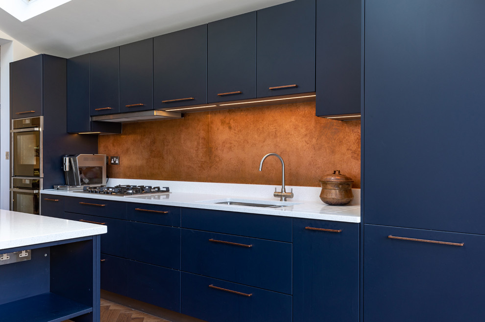 Idee per una grande cucina minimal con lavello sottopiano, ante lisce, ante blu, top in quarzite, paraspruzzi a effetto metallico, elettrodomestici neri, pavimento in legno massello medio, pavimento marrone e top bianco