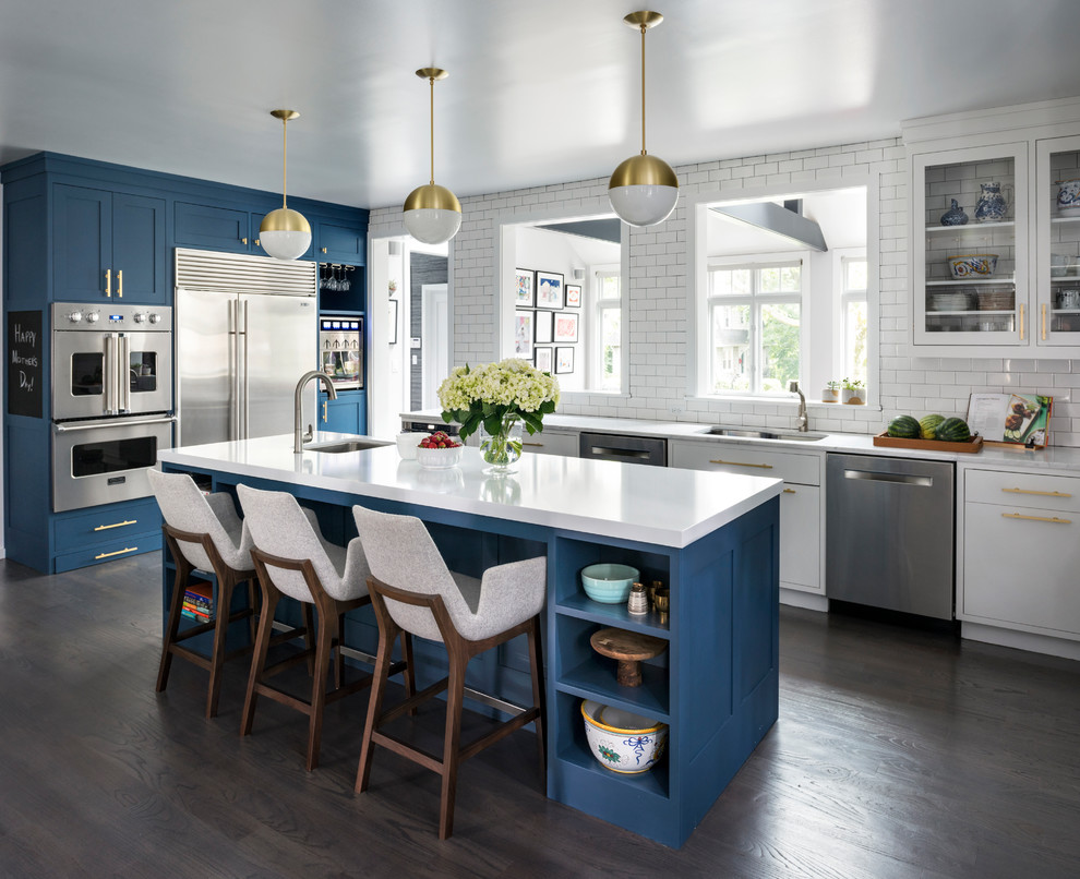 Kitchen - large transitional l-shaped brown floor and dark wood floor kitchen idea in New York with a double-bowl sink, shaker cabinets, blue cabinets, quartz countertops, white backsplash, stainless steel appliances, an island and subway tile backsplash