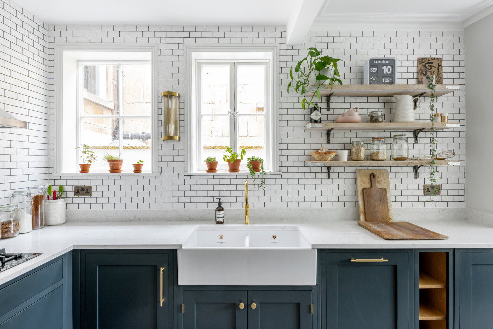 Design ideas for a large eclectic l-shaped open plan kitchen in Other with a belfast sink, shaker cabinets, blue cabinets, composite countertops, white splashback, metro tiled splashback, black appliances, concrete flooring, a breakfast bar, grey floors and white worktops.