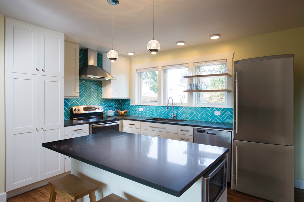 На фото: кухня с синим фартуком, фартуком из стеклянной плитки, островом, одинарной мойкой, белыми фасадами, светлым паркетным полом и коричневым полом