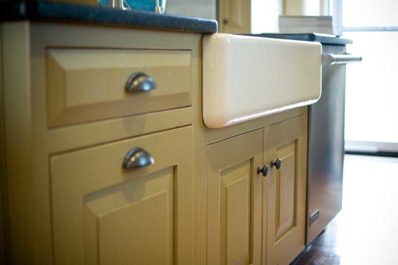 Bild på ett lantligt kök, med en rustik diskho, luckor med upphöjd panel, gröna skåp, granitbänkskiva, vitt stänkskydd, stänkskydd i keramik, rostfria vitvaror, ljust trägolv och en köksö