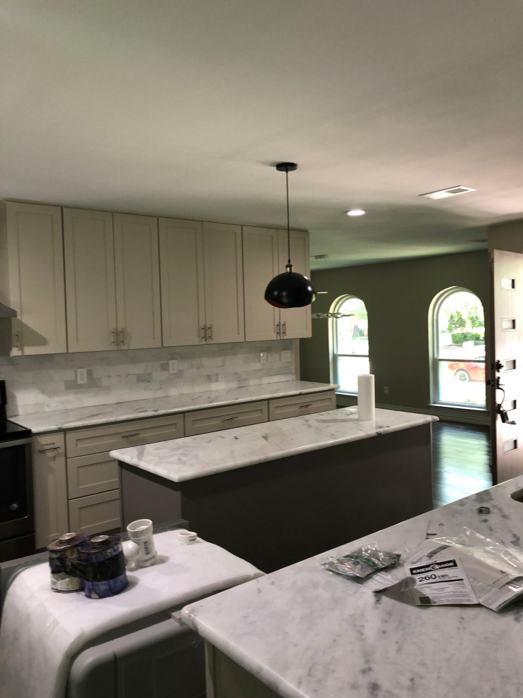 Modern inredning av ett mellanstort vit vitt kök och matrum, med en dubbel diskho, skåp i shakerstil, beige skåp, marmorbänkskiva, vitt stänkskydd, stänkskydd i stenkakel, rostfria vitvaror, ljust trägolv, en köksö och brunt golv