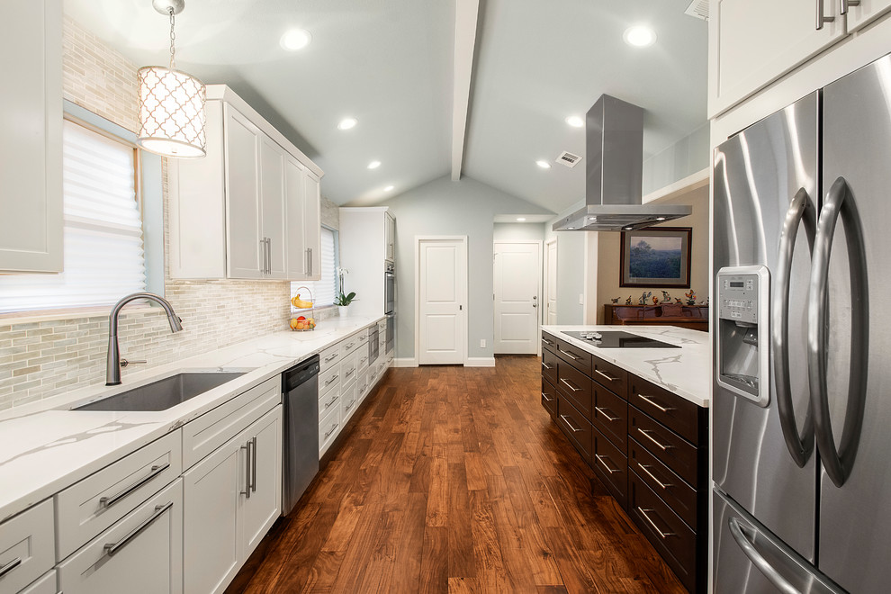 Bild på ett mellanstort vintage vit vitt kök, med en undermonterad diskho, släta luckor, vita skåp, bänkskiva i kvarts, stänkskydd med metallisk yta, stänkskydd i glaskakel, rostfria vitvaror, mellanmörkt trägolv, en halv köksö och brunt golv