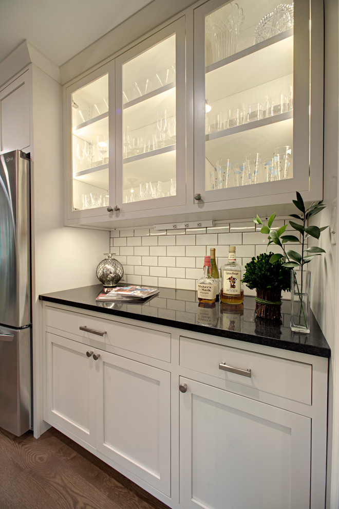 Example of a trendy dark wood floor kitchen design in Chicago with glass-front cabinets, white cabinets, white backsplash, subway tile backsplash and stainless steel appliances