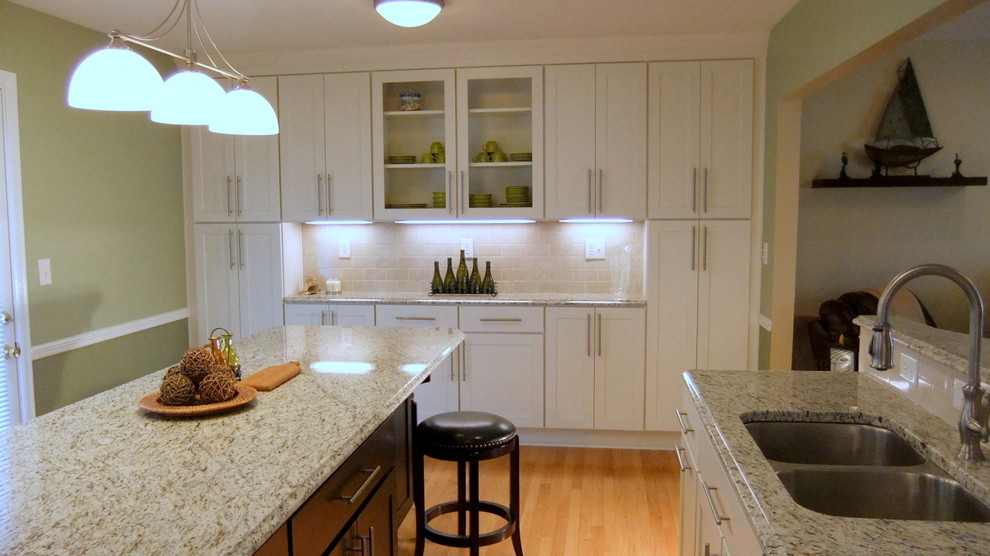 Mid-sized trendy l-shaped medium tone wood floor eat-in kitchen photo in Other with an undermount sink, shaker cabinets, white cabinets, granite countertops, beige backsplash, subway tile backsplash, stainless steel appliances and an island