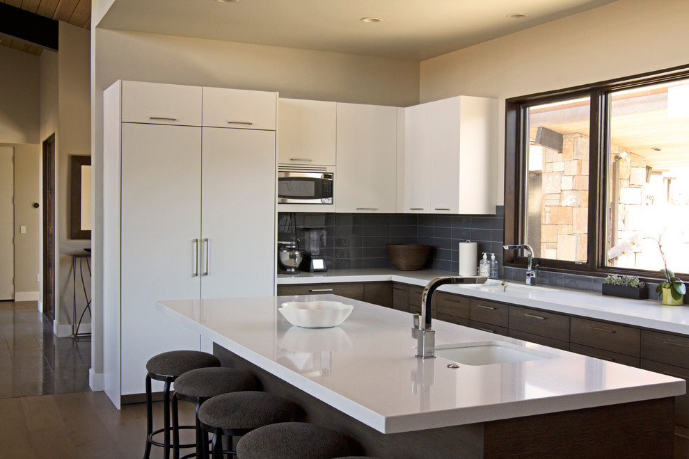 Large contemporary u-shaped enclosed kitchen in Salt Lake City with a submerged sink, flat-panel cabinets, white cabinets, composite countertops, grey splashback, metro tiled splashback, integrated appliances, dark hardwood flooring and an island.