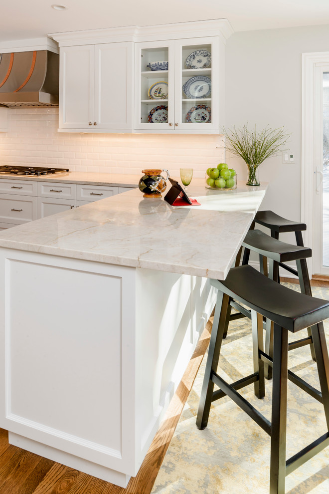 Eat-in kitchen - large transitional medium tone wood floor eat-in kitchen idea in Chicago with a farmhouse sink, shaker cabinets, white cabinets, quartzite countertops, white backsplash, ceramic backsplash, stainless steel appliances and an island