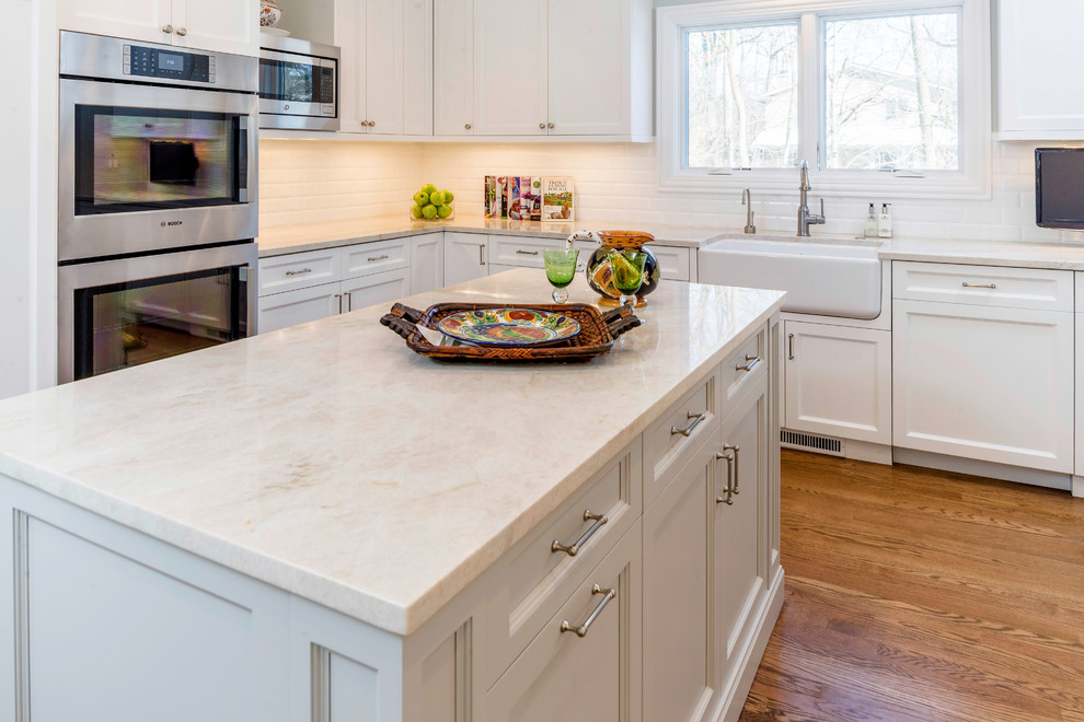 Large transitional medium tone wood floor eat-in kitchen photo in Chicago with a farmhouse sink, shaker cabinets, white cabinets, quartzite countertops, white backsplash, ceramic backsplash, stainless steel appliances and an island