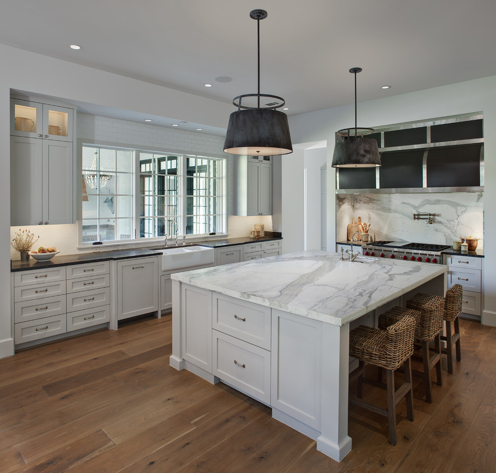 Large transitional u-shaped medium tone wood floor and brown floor enclosed kitchen photo in Houston with a farmhouse sink, shaker cabinets, white cabinets, marble countertops, white backsplash, subway tile backsplash, stainless steel appliances and an island