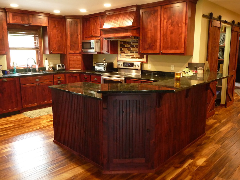Klassisk inredning av ett mellanstort kök, med en undermonterad diskho, granitbänkskiva, ljust trägolv, skåp i shakerstil, rostfria vitvaror, skåp i mörkt trä, flerfärgad stänkskydd, stänkskydd i glaskakel, en halv köksö och brunt golv
