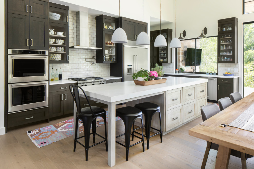 Example of a farmhouse l-shaped light wood floor and beige floor open concept kitchen design in Denver with an undermount sink, shaker cabinets, dark wood cabinets, white backsplash, stainless steel appliances, an island and white countertops