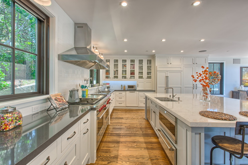 Example of a huge u-shaped light wood floor open concept kitchen design in Los Angeles with a double-bowl sink, recessed-panel cabinets, white cabinets, white backsplash, subway tile backsplash, stainless steel appliances and an island