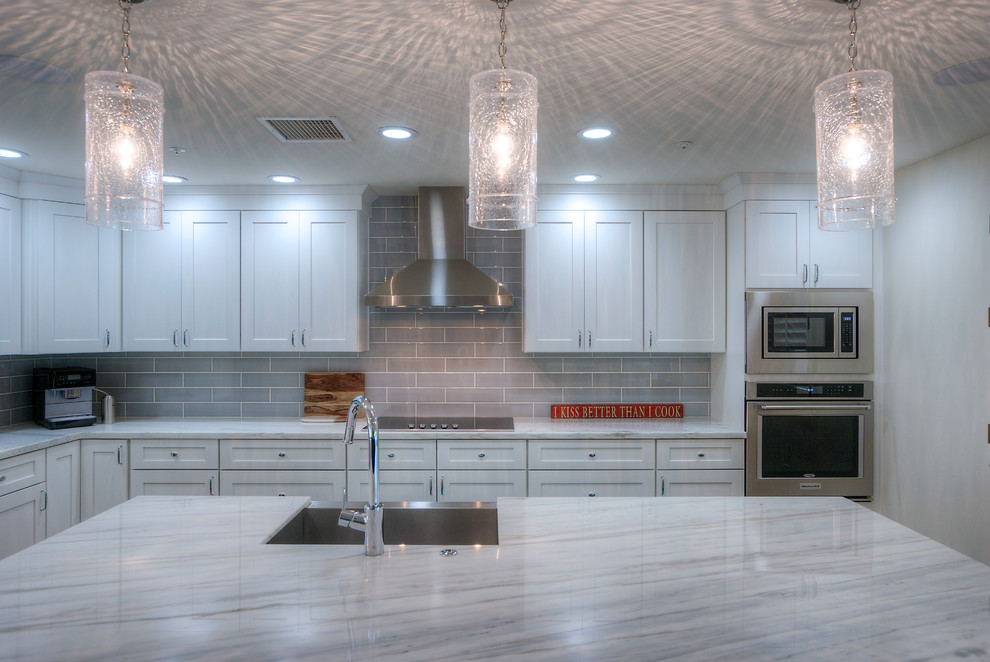 Example of a mid-sized minimalist u-shaped medium tone wood floor eat-in kitchen design with a drop-in sink, beaded inset cabinets, white cabinets, marble countertops, gray backsplash, subway tile backsplash, stainless steel appliances and an island