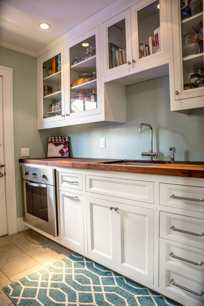 This is an example of a traditional galley kitchen pantry in San Diego with a submerged sink, recessed-panel cabinets, white cabinets, wood worktops, limestone flooring and an island.