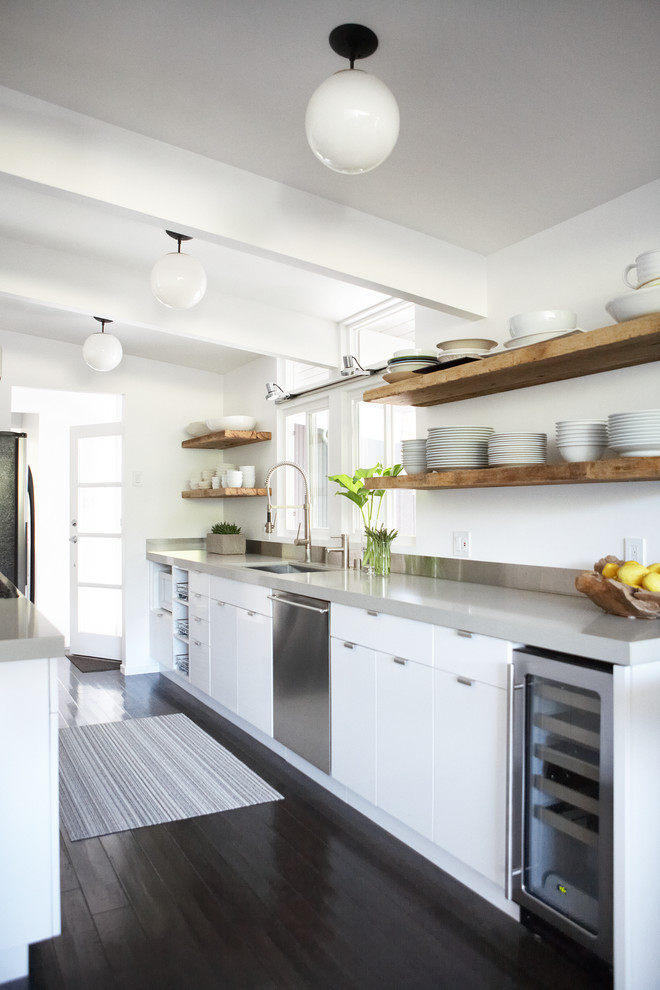 Modelo de cocina contemporánea con fregadero bajoencimera, armarios con paneles lisos, puertas de armario blancas, electrodomésticos de acero inoxidable, suelo de madera oscura, suelo negro, encimeras grises y una isla