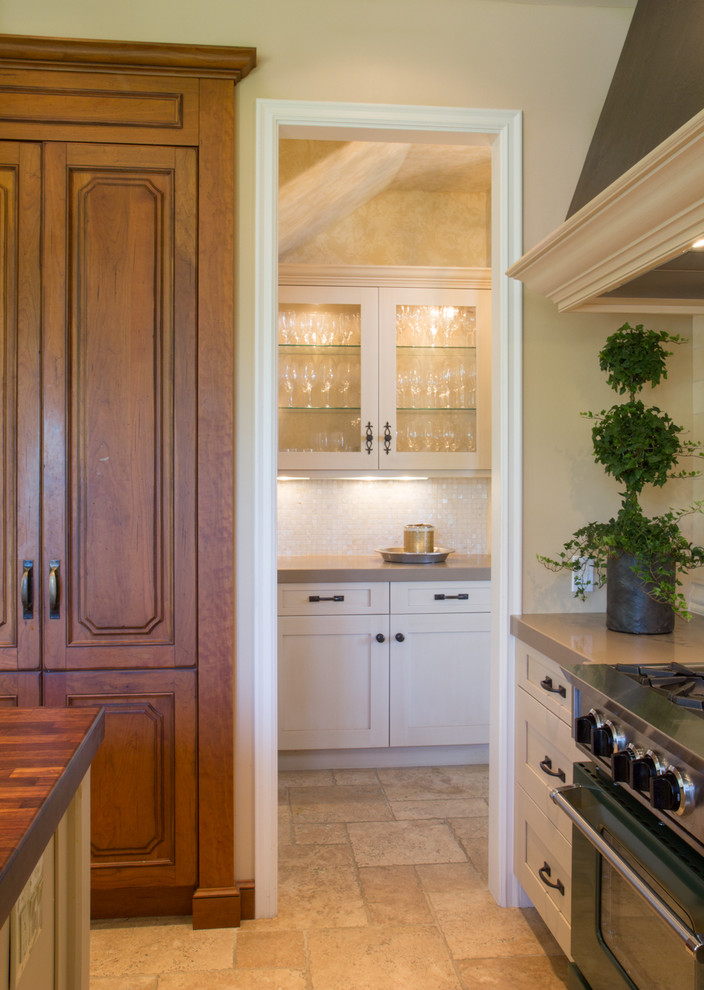 Photo of a transitional u-shaped eat-in kitchen in San Diego with a farmhouse sink, recessed-panel cabinets, medium wood cabinets, wood benchtops, beige splashback, ceramic splashback and white appliances.