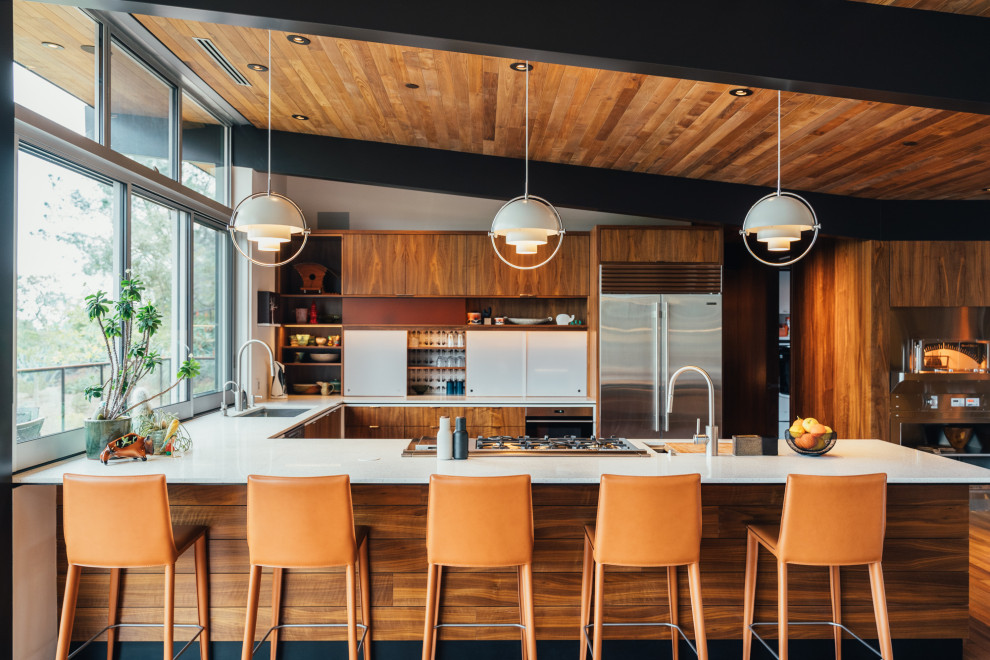 Inspiration for a midcentury u-shaped open plan kitchen in San Diego with a submerged sink, flat-panel cabinets, medium wood cabinets, stainless steel appliances, a breakfast bar, white worktops, exposed beams and a wood ceiling.