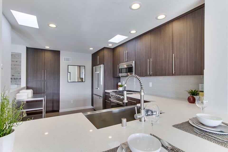 Inspiration for a mid-sized contemporary l-shaped light wood floor and gray floor open concept kitchen remodel in San Diego with a farmhouse sink, flat-panel cabinets, medium tone wood cabinets, quartz countertops, white backsplash, porcelain backsplash, stainless steel appliances and a peninsula