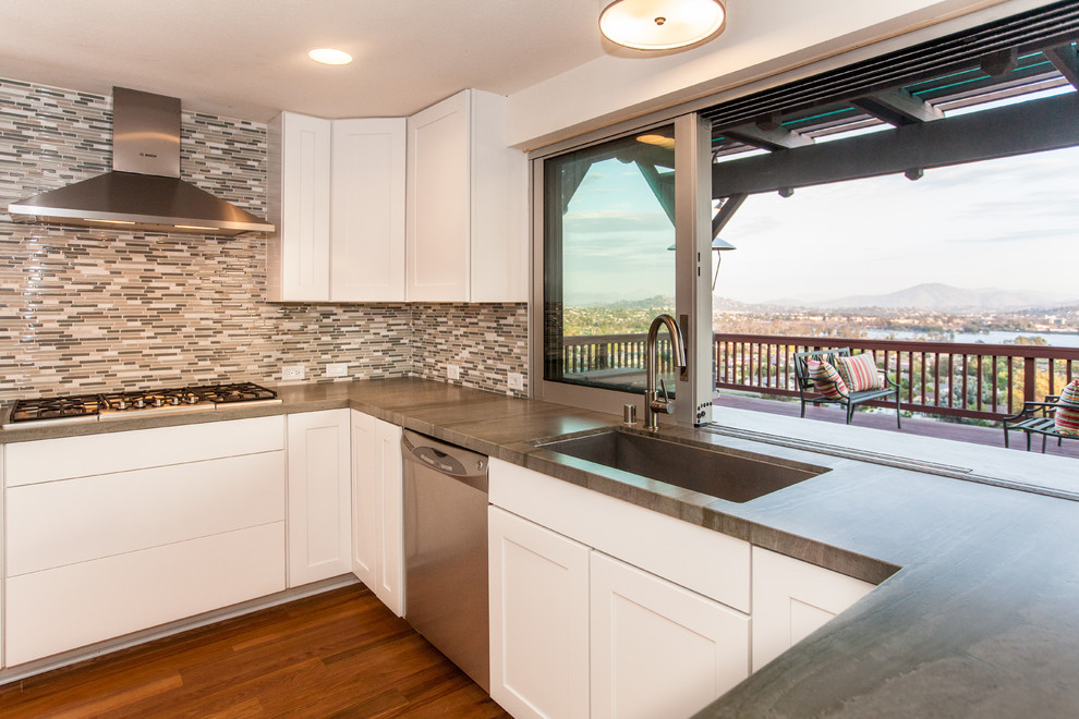Contemporary open plan kitchen in San Diego with a submerged sink, recessed-panel cabinets, white cabinets, multi-coloured splashback, ceramic splashback, stainless steel appliances, medium hardwood flooring and a breakfast bar.