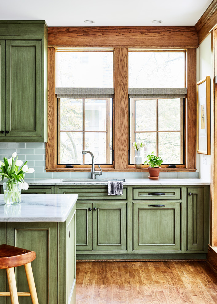 Inspiration för mellanstora amerikanska linjära grått kök med öppen planlösning, med en undermonterad diskho, luckor med infälld panel, gröna skåp, bänkskiva i kvarts, grönt stänkskydd, stänkskydd i glaskakel, integrerade vitvaror, mellanmörkt trägolv, en köksö och brunt golv