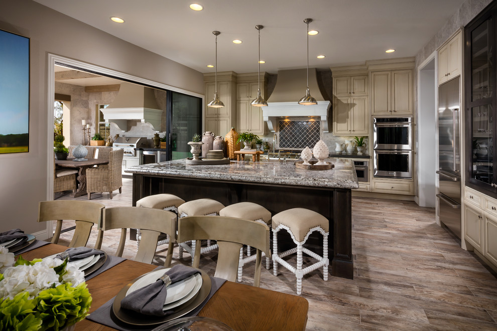 Example of a large tuscan eat-in kitchen design in Orange County with beige cabinets, granite countertops, gray backsplash, ceramic backsplash, stainless steel appliances, an island and multicolored countertops