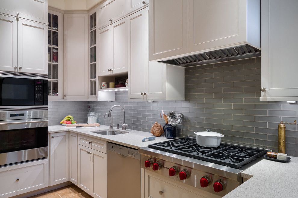 Modern inredning av ett avskilt, mellanstort u-kök, med en undermonterad diskho, skåp i shakerstil, vita skåp, bänkskiva i kvarts, blått stänkskydd, stänkskydd i glaskakel, rostfria vitvaror, travertin golv, en köksö och brunt golv