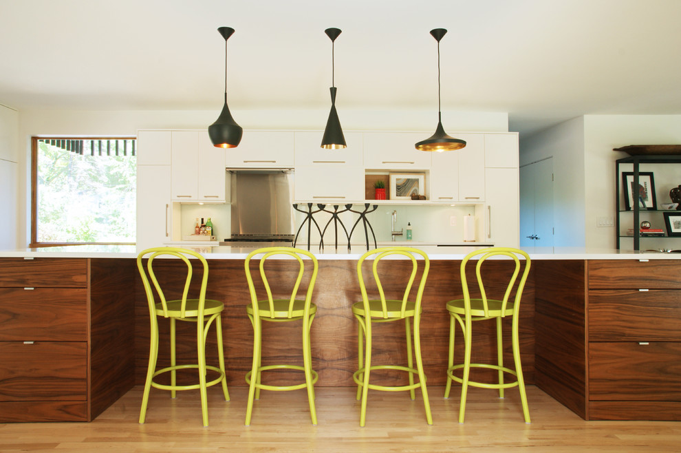 Foto på ett funkis kök, med släta luckor, vita skåp, vitt stänkskydd, glaspanel som stänkskydd, ljust trägolv och en köksö