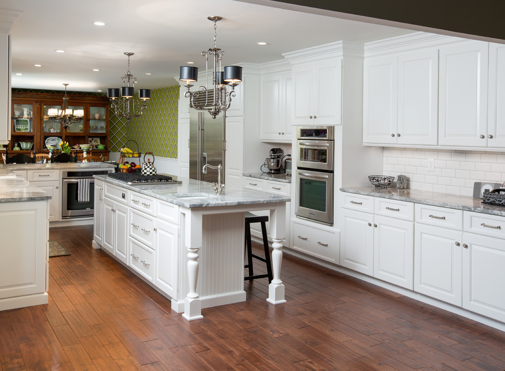 Inspiration for a large timeless u-shaped medium tone wood floor eat-in kitchen remodel in Columbus with a farmhouse sink, white cabinets, granite countertops, white backsplash, stainless steel appliances and an island