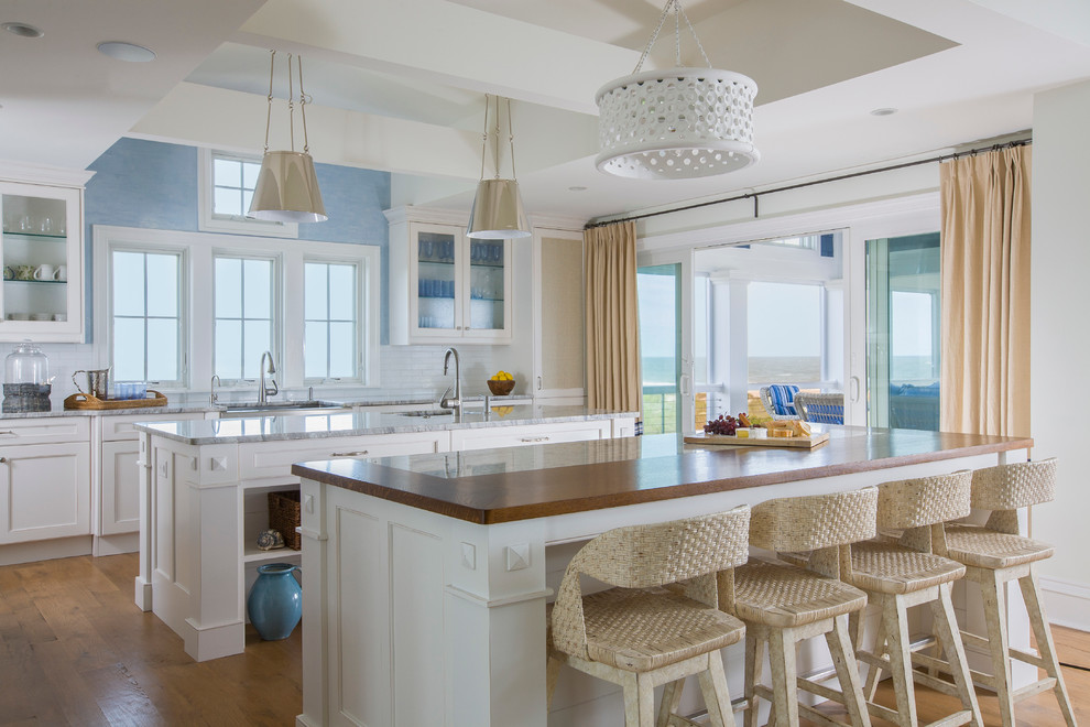 Example of a large beach style light wood floor and beige floor open concept kitchen design in Baltimore with two islands, an undermount sink, shaker cabinets, white cabinets, wood countertops and brown countertops