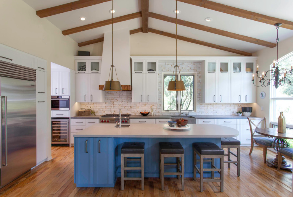 Example of a mid-sized country l-shaped medium tone wood floor and brown floor open concept kitchen design in Denver with a farmhouse sink, white cabinets, quartz countertops, white backsplash, subway tile backsplash, stainless steel appliances, an island, gray countertops and recessed-panel cabinets