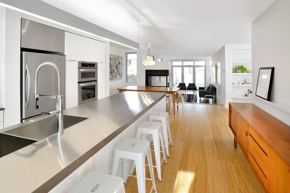 Ejemplo de cocina contemporánea abierta con fregadero integrado, encimera de acero inoxidable, armarios con paneles lisos y puertas de armario blancas