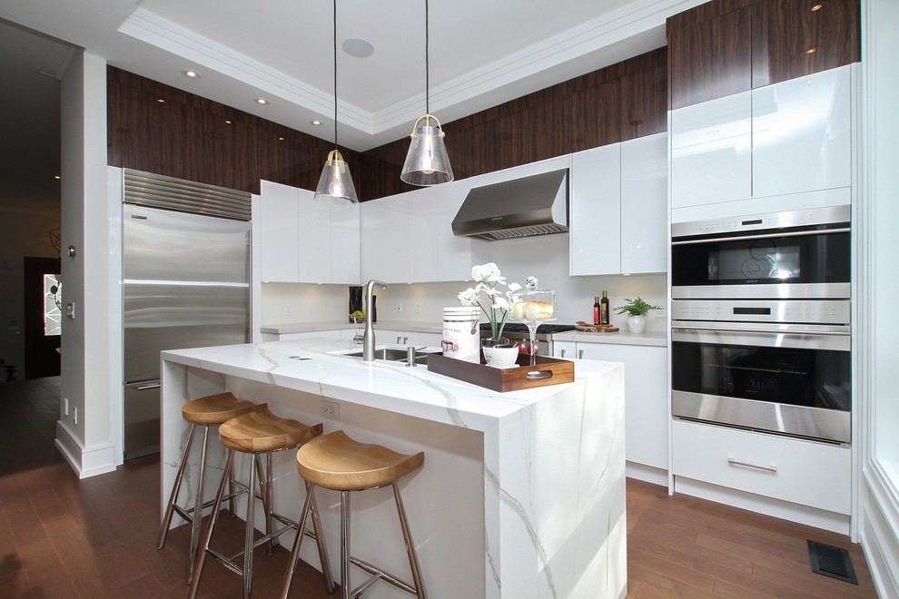 Trendy l-shaped medium tone wood floor kitchen photo in Toronto with a double-bowl sink, flat-panel cabinets, white cabinets, white backsplash, stainless steel appliances, an island and gray countertops