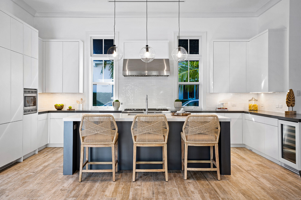 Inspiration for a contemporary u-shaped kitchen in Miami with a submerged sink, flat-panel cabinets, white cabinets, white splashback, integrated appliances, medium hardwood flooring, an island, brown floors and black worktops.