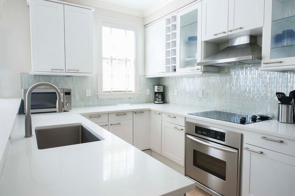 Bild på ett mellanstort maritimt kök, med en nedsänkt diskho, skåp i shakerstil, vita skåp, bänkskiva i kvarts, vitt stänkskydd, stänkskydd i glaskakel, rostfria vitvaror och travertin golv